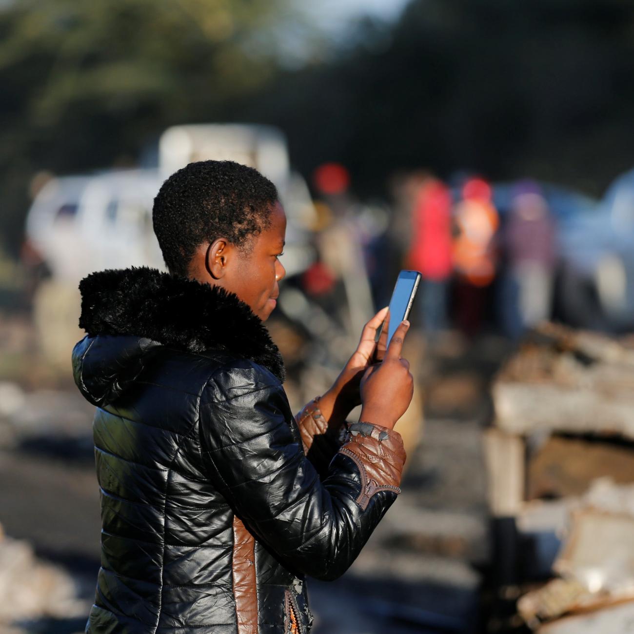 A woman uses her phone to take pictures of the wreckages of cars burnt after an accident involving a tanker.