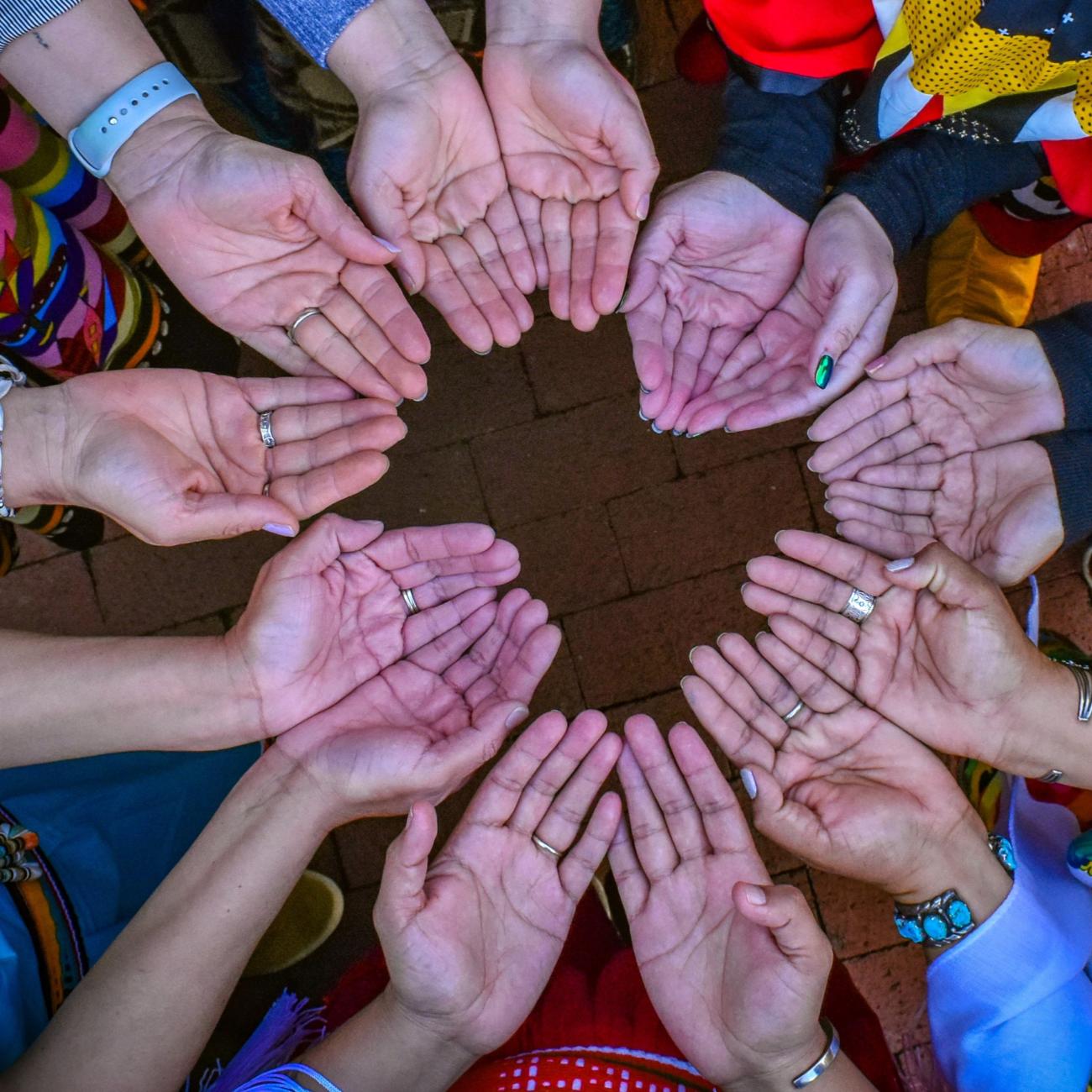 Changing Woman Initiative board and staff members, wearing traditional clothing from their respective tribes, connect with open hands to symbolize their acceptance of prayers and blessings.