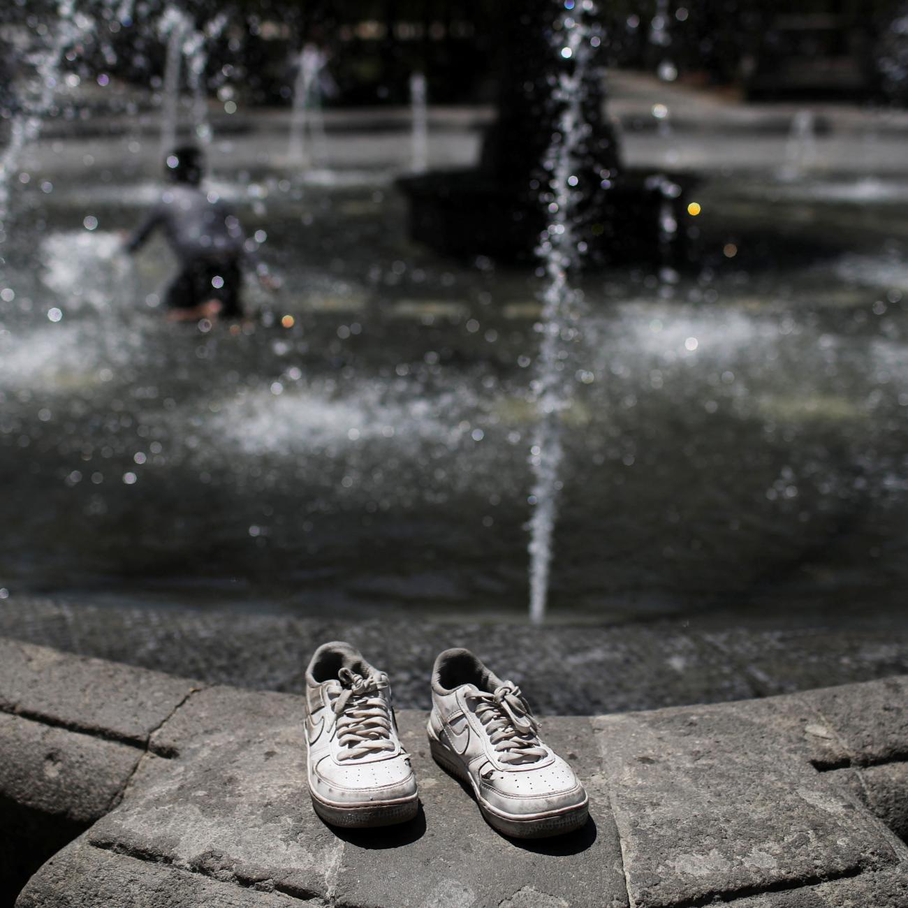 The tennis shoes rest on a fountain during a heat wave.