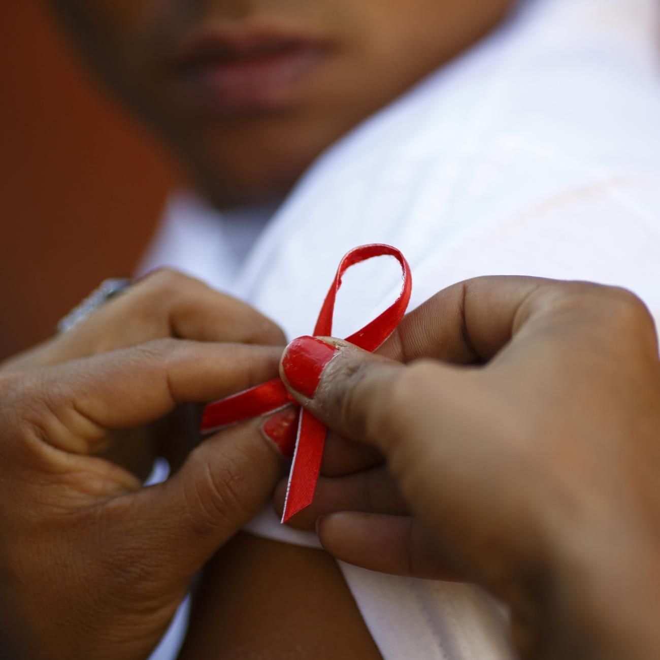 A red ribbon is put on the sleeves of a man by his friend to show support for people living with HIV, in Kathmandu, Nepal, on December 1, 2013.