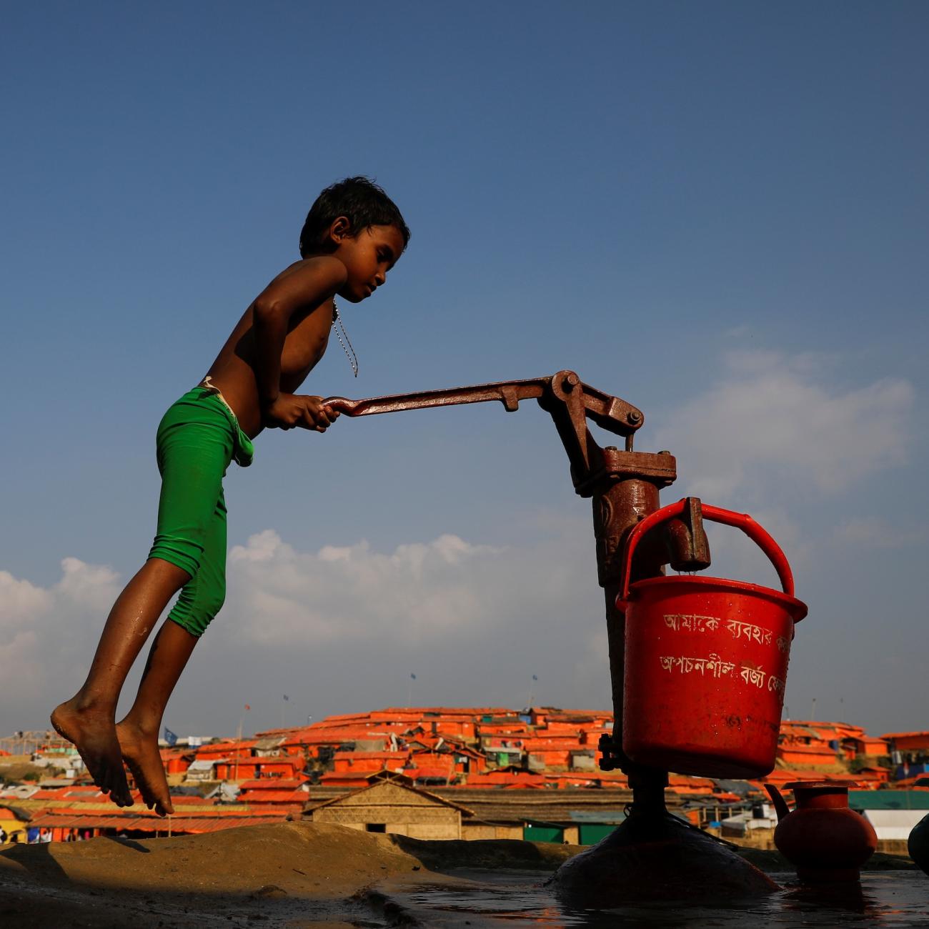 A Rohingya refugee child fills a bucket of water in Bangladesh.