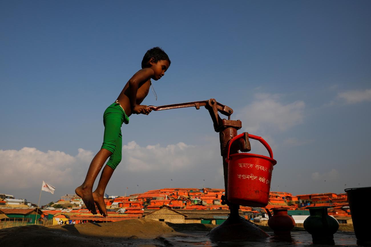 A Rohingya refugee child fills a bucket of water in Bangladesh.