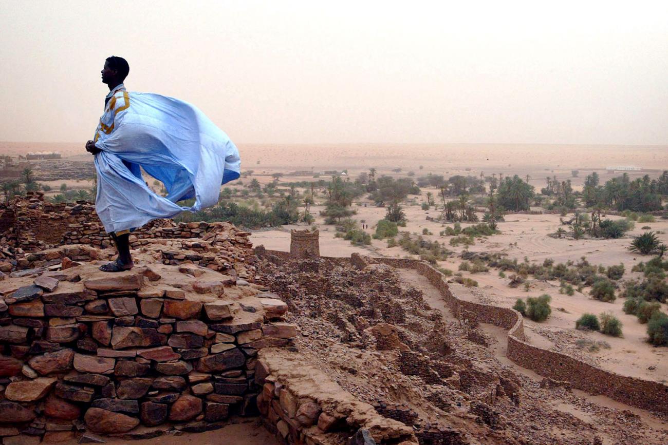 A Mauritanian man stands on what appears to be an ancient wall of old baked bricks on Aug 16, 2005 in the ancient village of Ouadane. He is wearing a light blue robe that is filling with strong winds, presumably carrying sand and dust south from the Sahara, and stands in bright contrast to the dull red background. Africa’s Sahel region is threatened by desertification. REUTERS/Finbarr O'Reilly