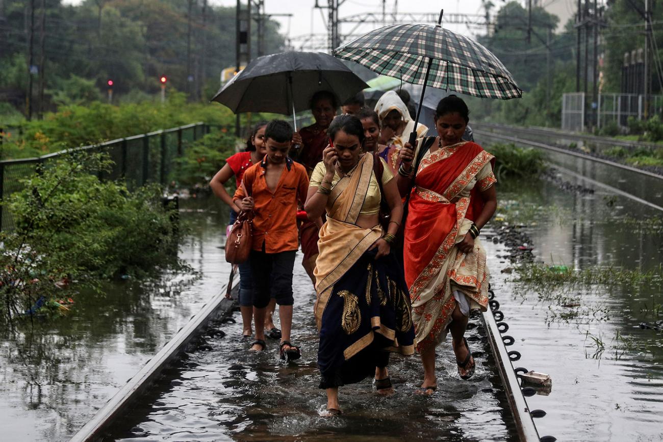 Commuters walk on waterlogged railway tracks after getting off a stalled train during heavy monsoon rains in Mumbai, India, on July 2, 2019. Several women and at least one boy are walking in a group. One of them is talking on a cell phone. Several are sharing umbrellas. The water, even on the train tracks, which are presumably slightly elevated, is up to their ankles. REUTERS/Francis Mascarenhas