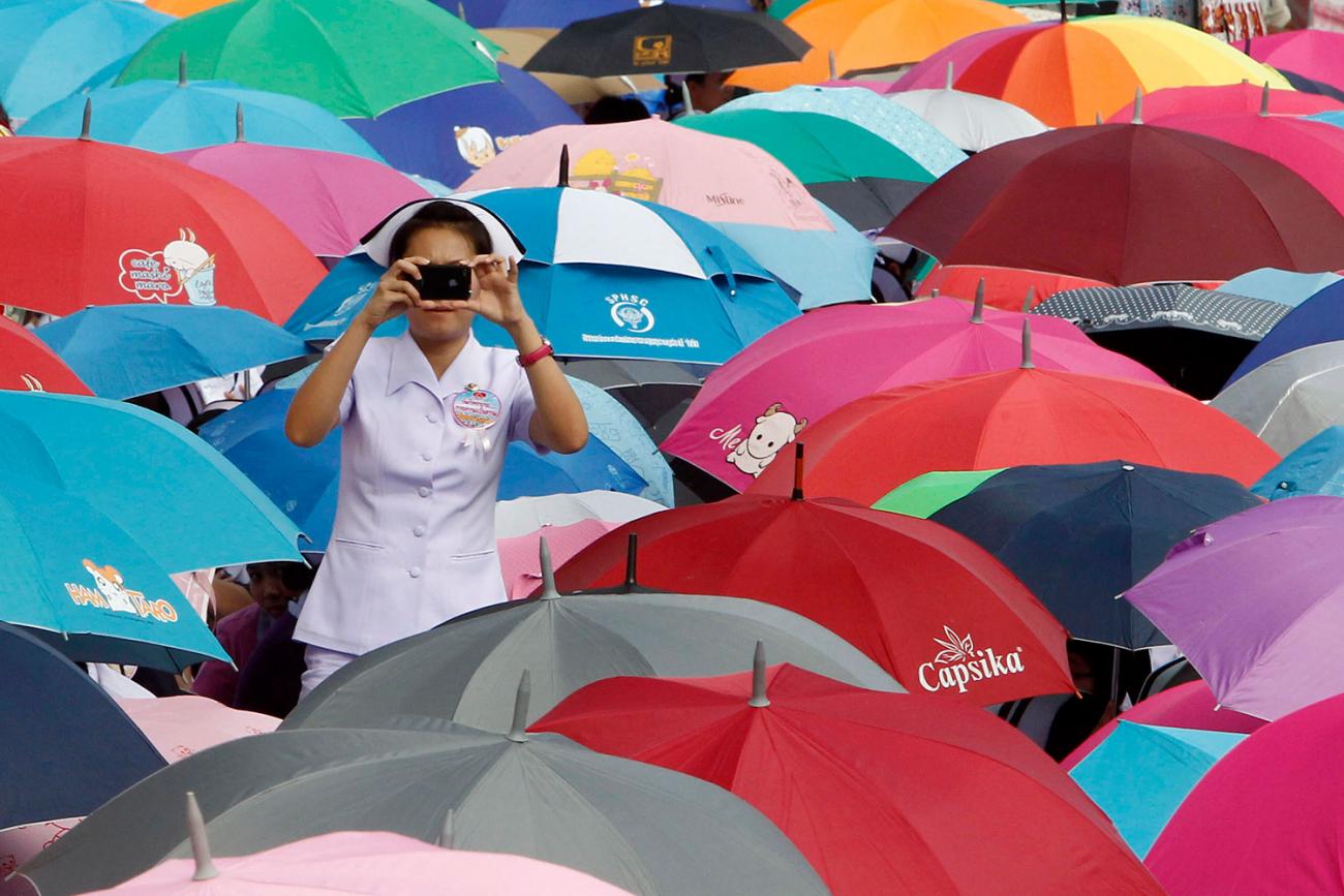 A nurse takes a photograph during a rally in front of the Government House in Bangkok October 16, 2012. Nurses attending the rally demanded better working conditions and full-time jobs, asking the government to improve job security by offering permanent contracts. The nurse stands in her white outfit against a sea of brightly colored umbrellas.