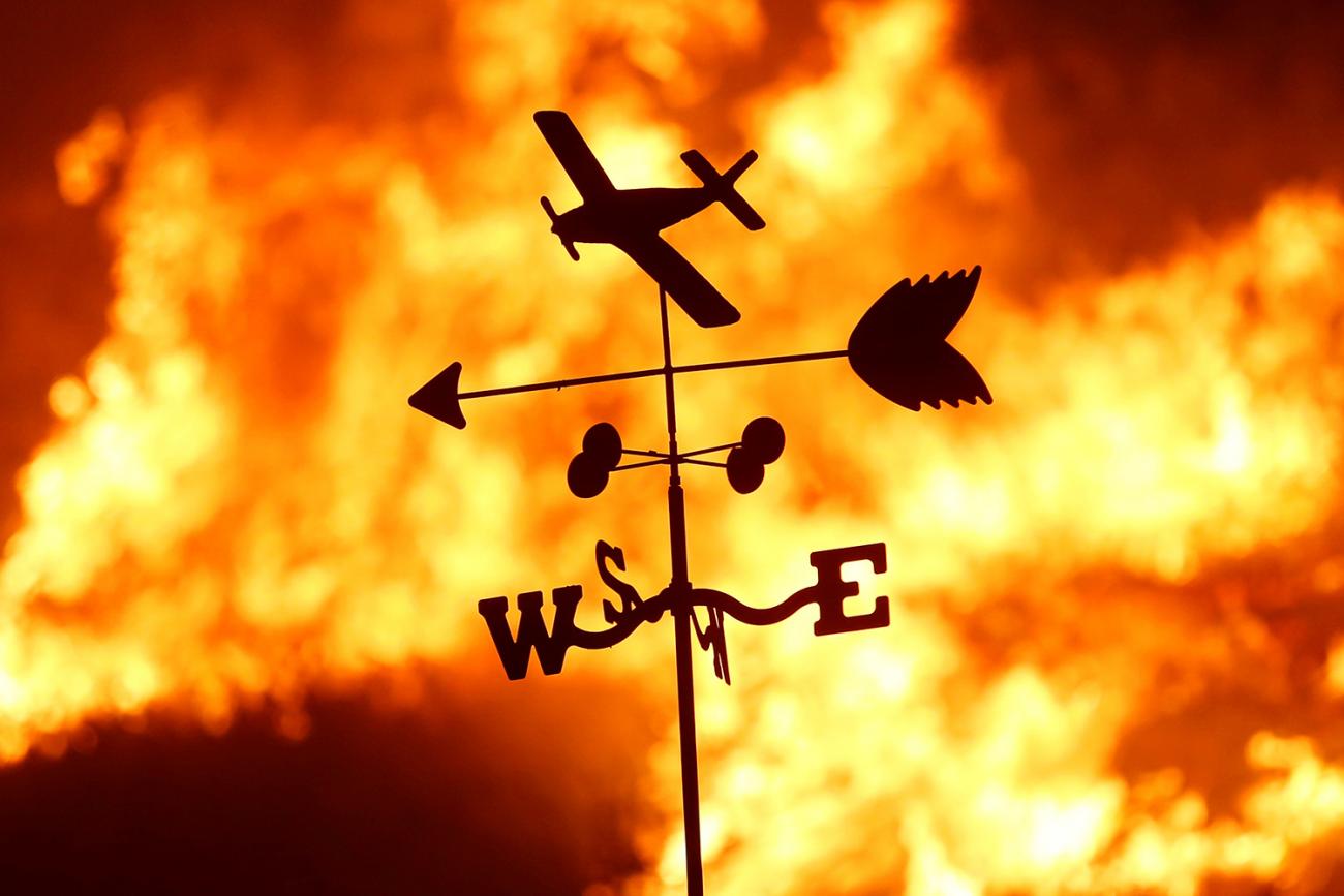 A weather vane is pictured on a ranch during the Creek Fire in the San Fernando Valley north of Los Angeles, in Sylmar, California on December 5, 2017. Picture shows a thin metal toy-like vain with a plane, and arrow and a “NESW” directional indicator silhouetted against a burning fire. REUTERS/Jonathan Alcorn