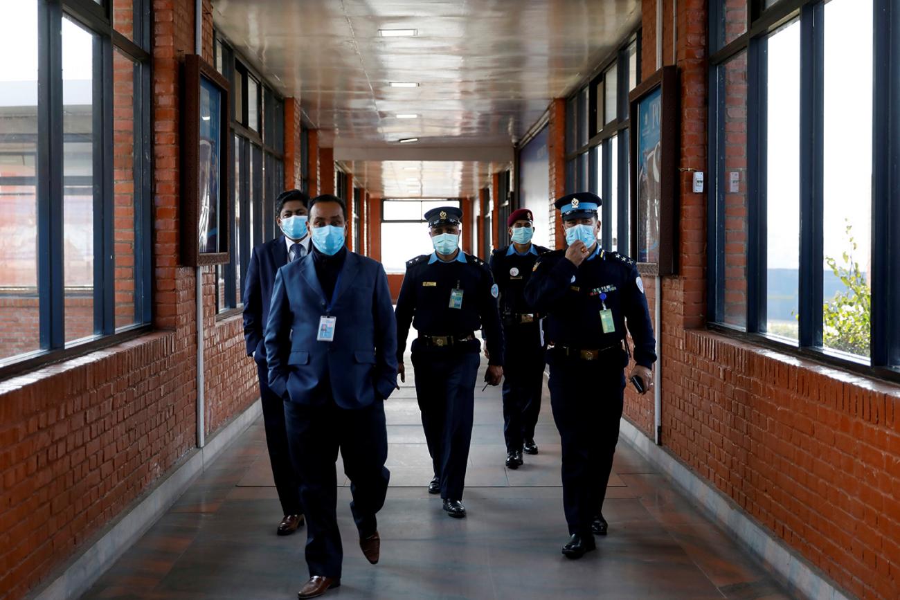 Nepalese police officers and other officials walking inside the Tribhuvan International Airport in Kathmandu after Nepal confirmed the first case of coronavirus in the country on January 28, 2020. The picture shows three officers in full uniforms and two officials wearing suits walking toward the camera down a long air terminal corridor with windows on both sides. REUTERS/Navesh Chitrakar.