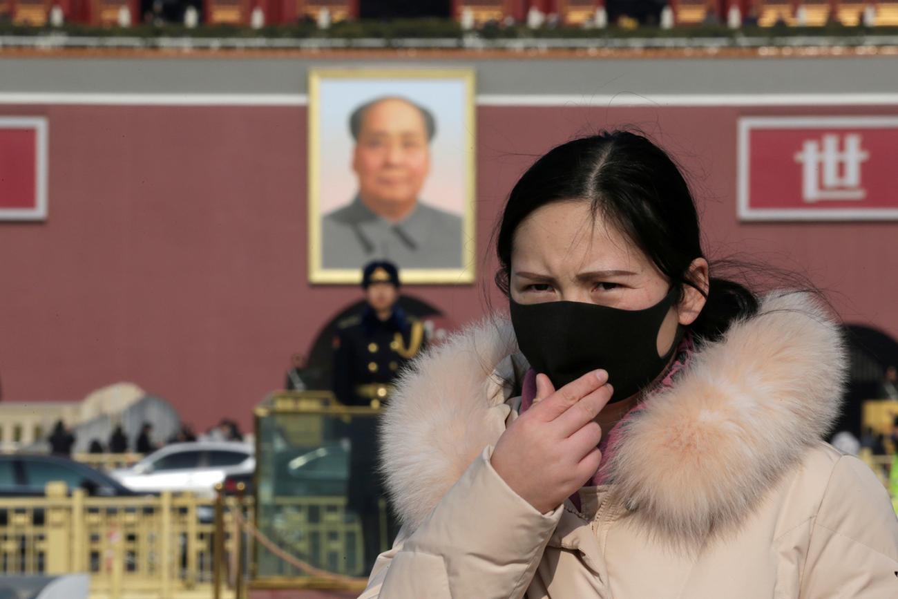 A tourist wearing a mask visits Tiananmen Square in Beijing, China January 22, 2020. The photo shows a woman in a black mask in the foreground with a huge portrait of Chairman Mao visible in the background, along with a uniformed officer standing guard. REUTERS/Jason Lee