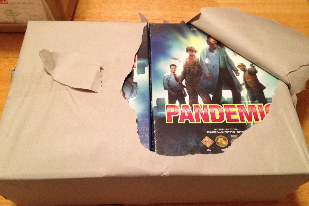 A bundle of the original Pandemic board game boxes. Photo a large armful-sized package neatly wrapped in brown paper. The paper is slightly torn open, revealing eight new boxes of the game Pandemic. Photo courtesy of Matt Leacock