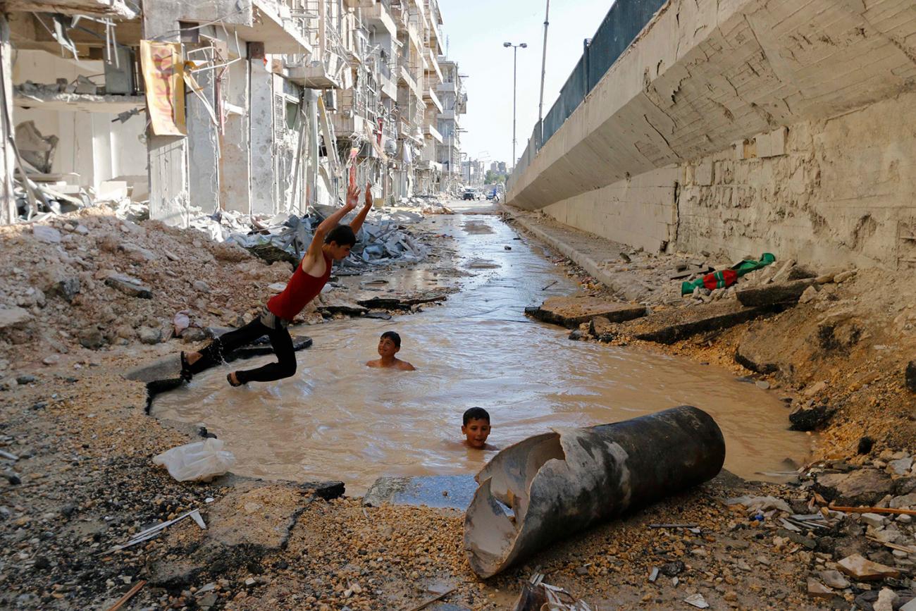 A boy dives into a crater filled with water in Aleppo's al-Shaar district on July 10, 2014. Activists said the crater was caused by barrel bombs dropped by forces of Syria's President Bashar al-Assad. The photo shows a boy leaping in mid-air into a water-filled hole. The water is muddy brown, and two other boys can be seen swimming in the hole with their heads bobbing out. Surrounding them is rubble. This is a powerful image. REUTERS/Hosam Katan