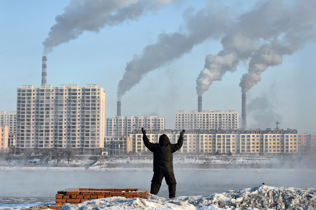Factories emit smoke in Jilin province, China, across the Songhua River from where an elderly man exercises on the morning of Feb 24, 2013, after Chinese authorities announced plans to curb pollution. The photo shows the man in the foreground, back to the camera, with buildings on the other side of the river pouring out smoke. REUTERS/Stringer