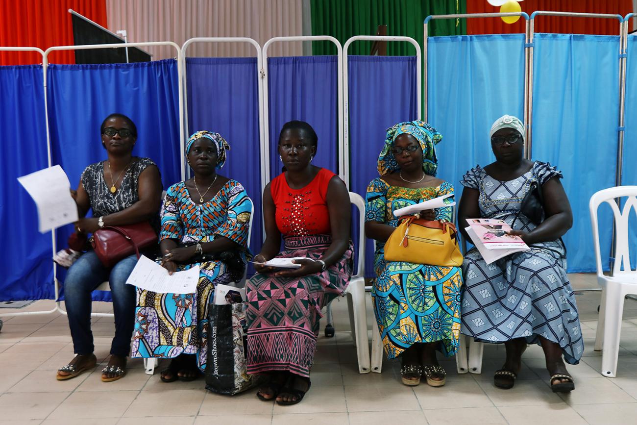 Women sit as they prepare for screenings during the breast cancer prevention campaign in Abidjan, Ivory Coast on October 12, 2019. Image shows a row of several women wearing colorful clothes. REUTERS/Luc Gnago