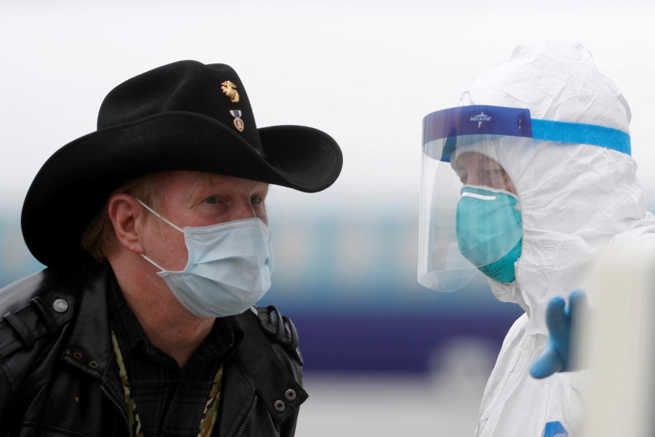 A worker in protective gear directs a masked passenger disembarking from the cruise ship Grand Princess in Oakland, California on March 10, 2020 amid concern over the growing COVID-19 pandemic. The picture shows a man wearing a mask and a cowboy hat standing facing a health worker in full protective gear. REUTERS/Stephen Lam 