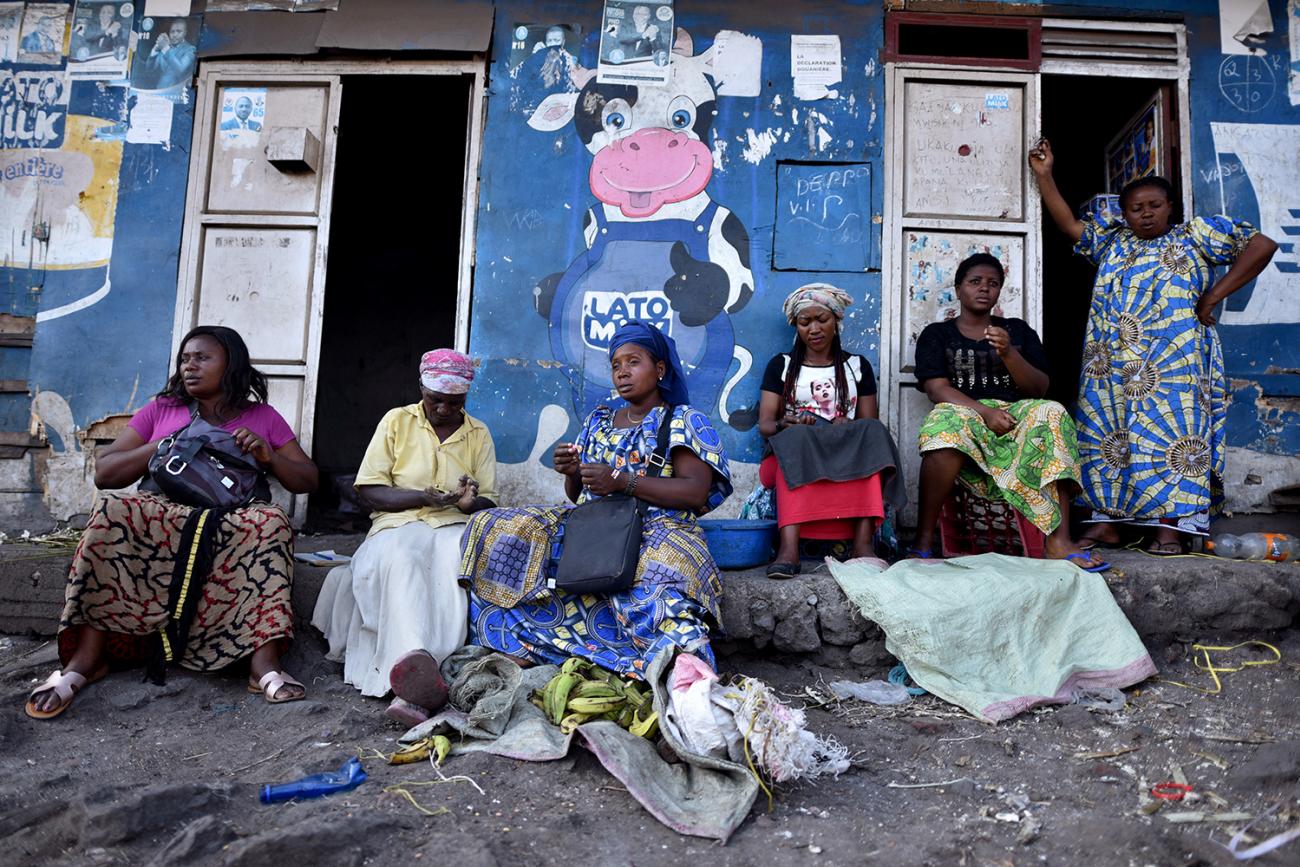 Traders sit near a deserted crossing point between Goma, Democratic Republic of Congo and Rwanda amid concerns about the spread of coronavirus on March 23, 2020. The photo shows a number of women sitting in front of a storefront painted blue and adorned by a large cartoon figure of a cow giving a thumb's up. REUTERS/Olivia Acland 