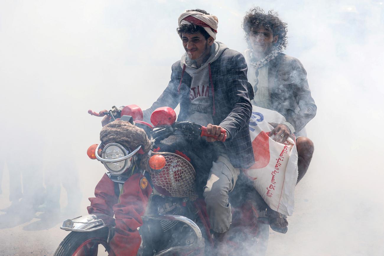 People ride a motorbike amidst smoke from fumigation during a fumigation campaign while the spread of the coronavirus disease (COVID-19) continues, on the outskirts of Sanaa, Yemen, on April 13, 2020. This is a powerful photo showing two men on one motorbike driving through a thick cloud of disinfectant mist. REUTERS/Khaled Abdullah