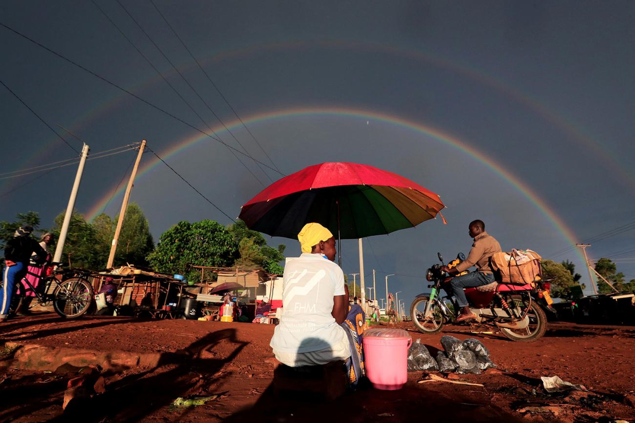 A double rainbow is seen above a woman holding an umbrella and selling snacks along the road in Siaya County, Kenya, on May 3, 2020, in the midst of the coronavirus pandemic. This is a spectacular photo that shows a woman under a bright red umbrella from behind as she is sitting on the side of the road greeting passer-bys with a full-double rainbow highlighting a storm-darkened sky in the distance. REUTERS/Thomas Mukoya