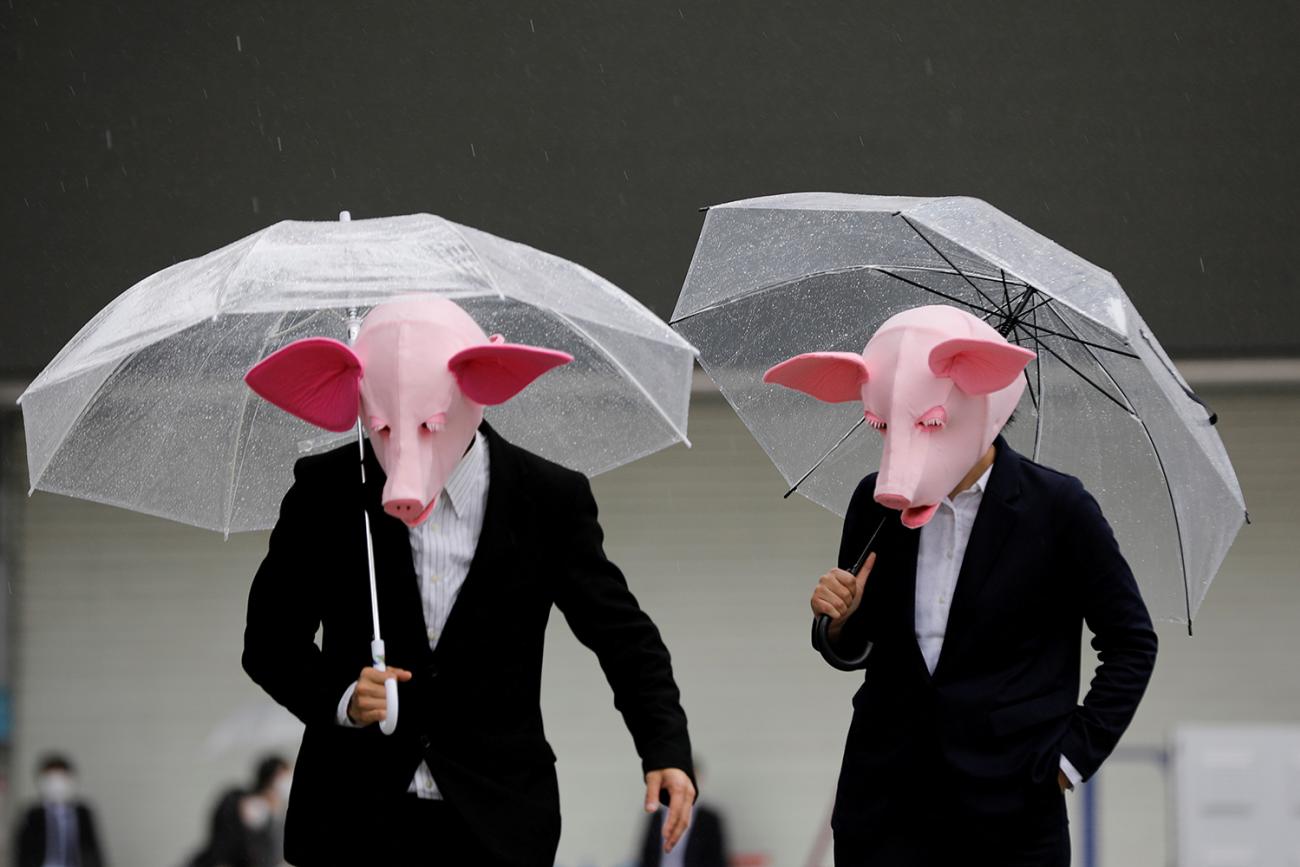 Youtubers wearing masks of pigs film a video at a shopping district, which has fewer people than usual amid the coronavirus outbreak in Tokyo, Japan, on May 19, 2020. The photo shows two people wearing pig masks and dark suits standing with clear plastic umbrellas open. REUTERS/Kim Kyung-Hoon 