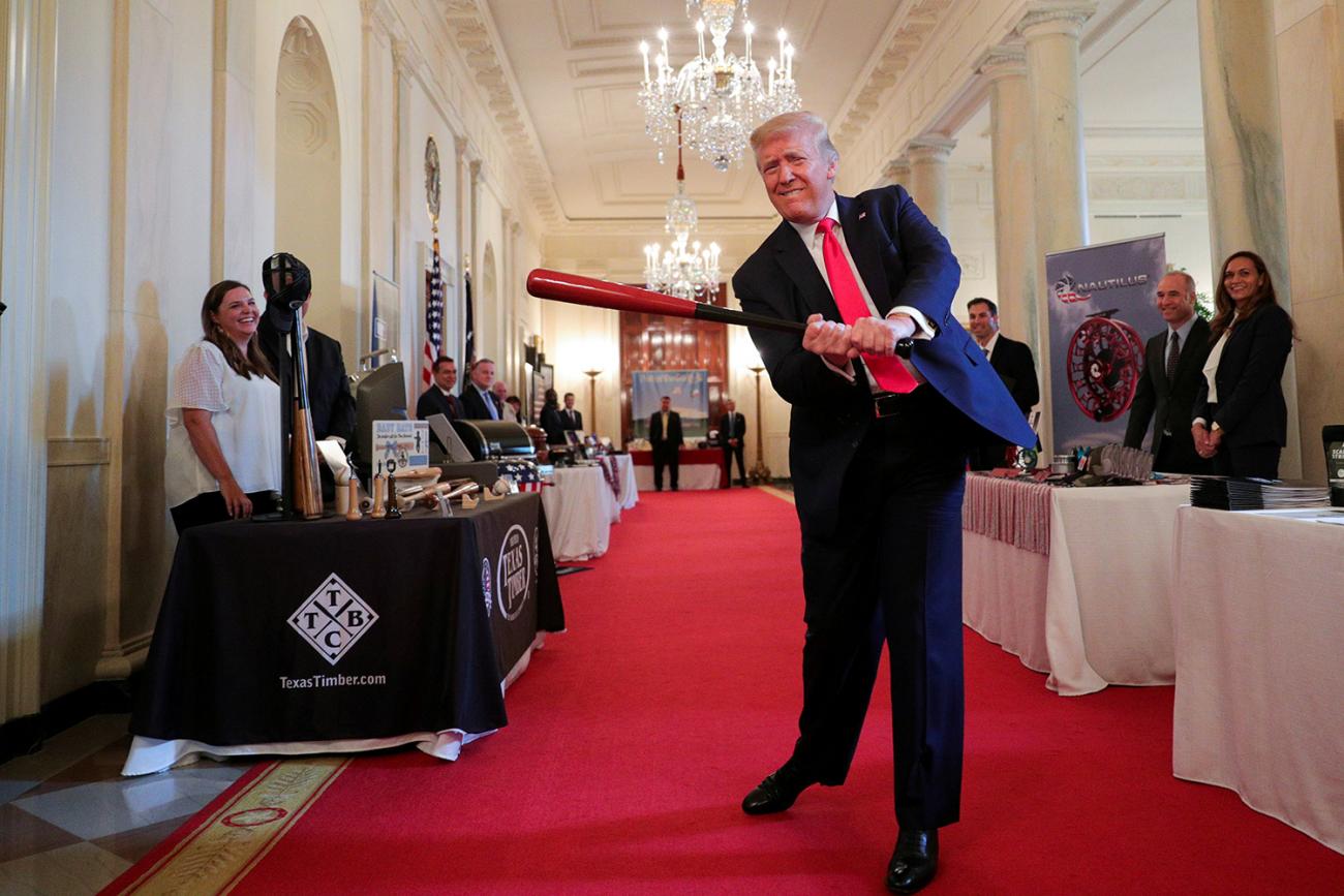 U.S. President Donald J. Trump swings a wooden baseball bat, celebrating a new jobs report, as he attends a "Spirit of America Showcase" event at the White House in Washington, DC, on July 2, 2020. The photo shows the president hamming it up with people staffing booths and swinging a red bat. REUTERS/Tom Brenner
