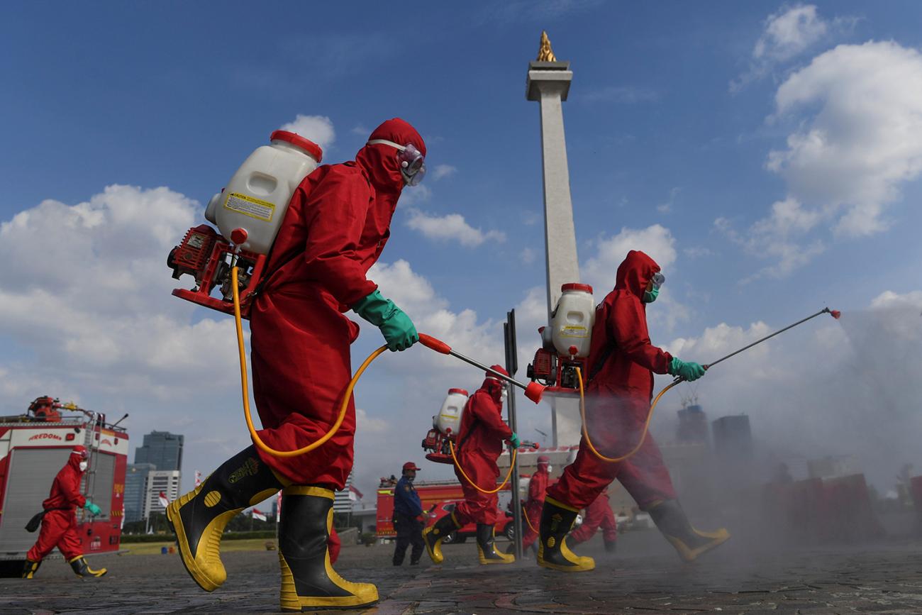 Firefighters wearing protective suits spray disinfectant at the National Monument area to prevent the spread of the coronavirus disease (COVID-19) in Jakarta, Indonesia, on June 17, 2020. Photo shows several workers in bright red protective suits walking though an open area spraying from tanks they carry on their backs. A monument can be seen in the background. REUTERS/Antara Foto/Wahyu Putro