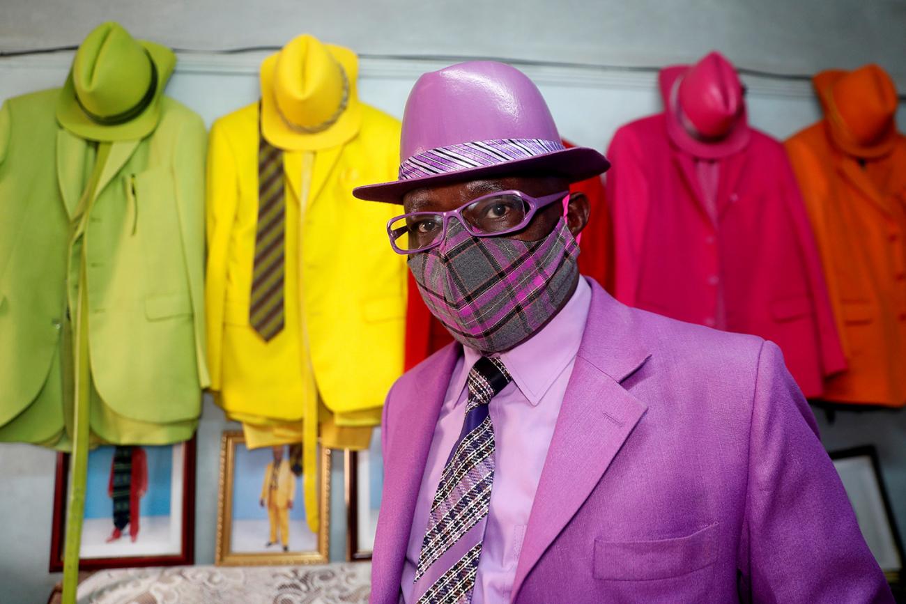 The author argues for pandemic responses that do not sacrifice long-term health projects—just as Kenyan fashionista James Maina Mwangi, on July 30, 2020, blends 160 stylish suits with sensible masks. Picture shows James smartly dressed in a well-appointed purple suit with a matching mask. In the background are striking blue and orange and green suits hanging on the wall. REUTERS/Thomas Mukoya