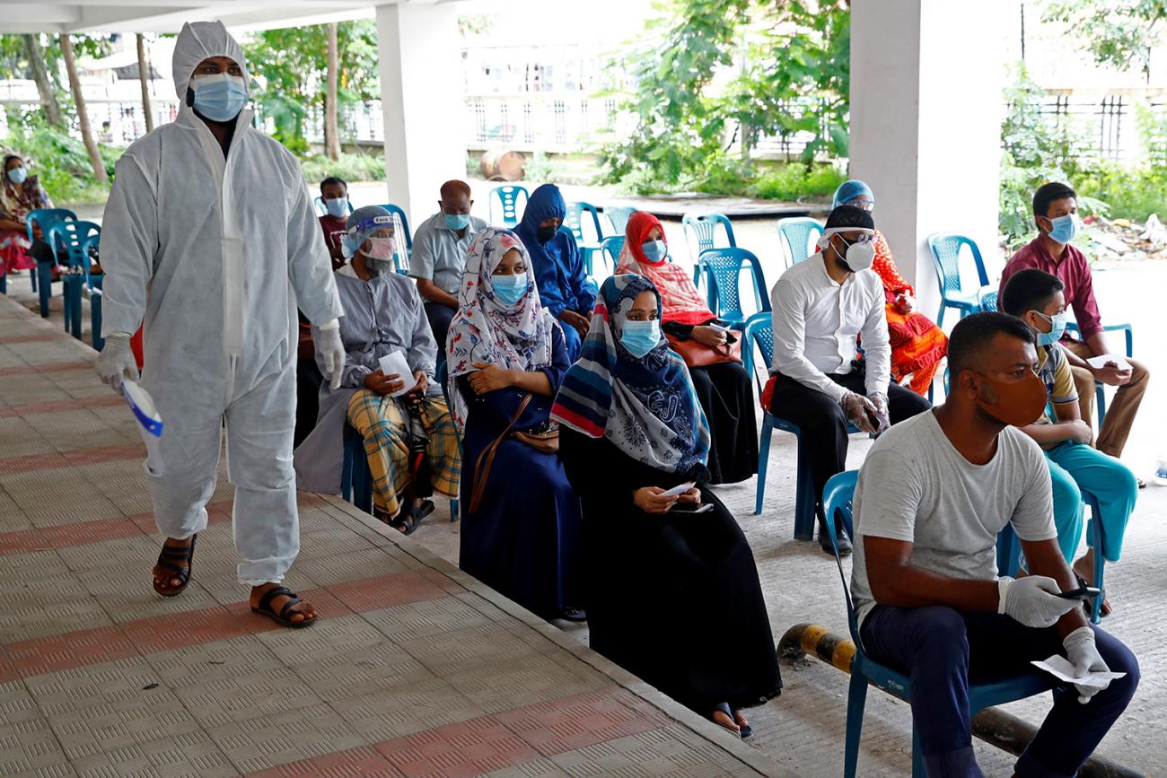 People at a coronavirus testing center on July 2, 2020 in Mugda Medical College in Dhaka, Bangladesh, where half of the medical equipment in public health facilities goes unused according to the authors. The photo shows a crowd of people wearing masks waiting on line in chairs while a health worker in full protective gear walks beside them. REUTERS/Mohammad Ponir Hossain