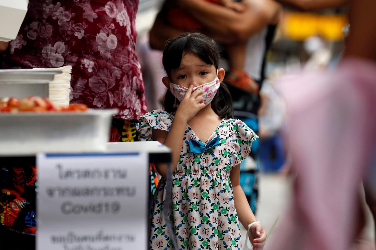 A girl from a migrant worker family that came to Thailand from Myanmar and lost their jobs due to COVID-19, lines up for free food in Bangkok, Thailand, on April 23, 2020. The photo shows a small girl wearing a facemask looking at the camera. REUTERS/Soe Zeya Tun