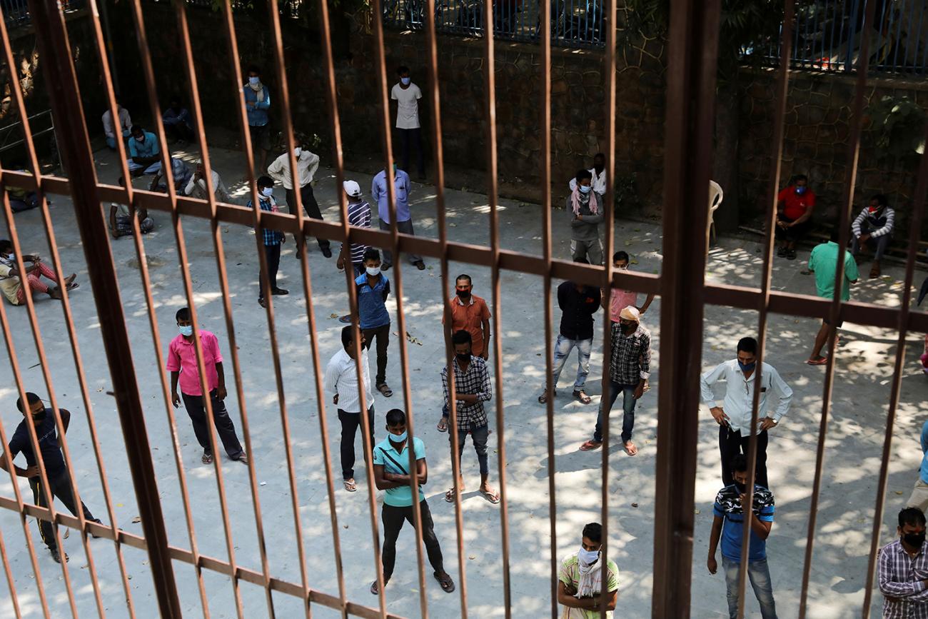 People wearing protective face masks wait for their rapid antigen test results outside a community center, amidst the spread of coronavirus in New Delhi, India, on September 17, 2020. The photo shows a large crowd of people from behind the bars of an iron fence. REUTERS/Anushree Fadnavis