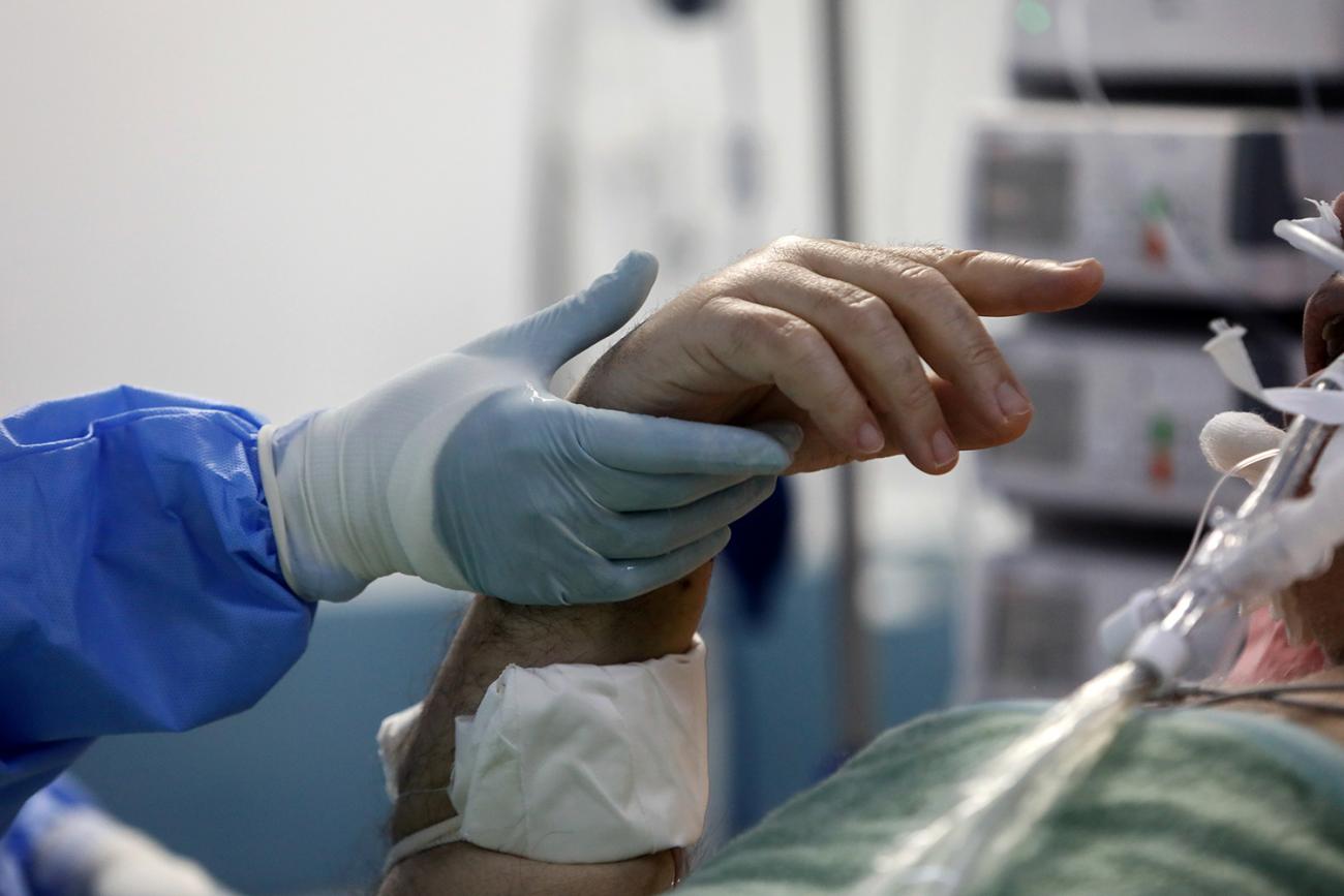 An intubated patient tries to gesture at a medical worker holding his hand at the Sotiria hospital ICU during the coronavirus outbreak, in Athens, Greece, on April 25, 2020. Picture shows the hand of a patient in a hospital bed being held by the blue-gloved hand of a medical worker. REUTERS/Giorgos Moutafis