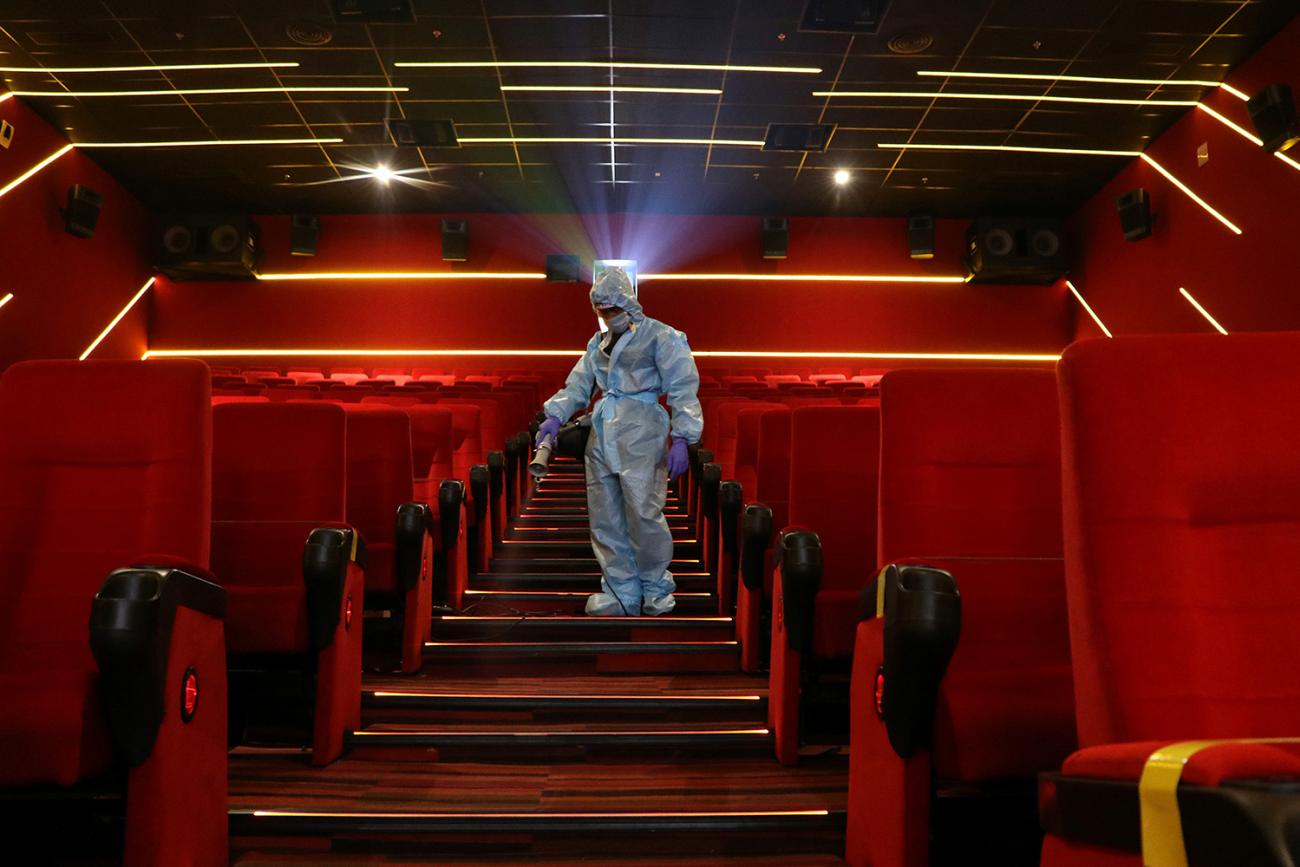 Addressing pandemic preparedness after COVID-19 will require going deeper than the surface. Here a worker sanitizes surfaces inside the Inox Leisure movie theatre in Mumbai, India, October 13, 2020. The photo is striking, showing a worker spraying disinfectant wearing a blue suit descending down a theater staircase where all the seats and carpet are bright red. REUTERS/Niharika Kulkarni