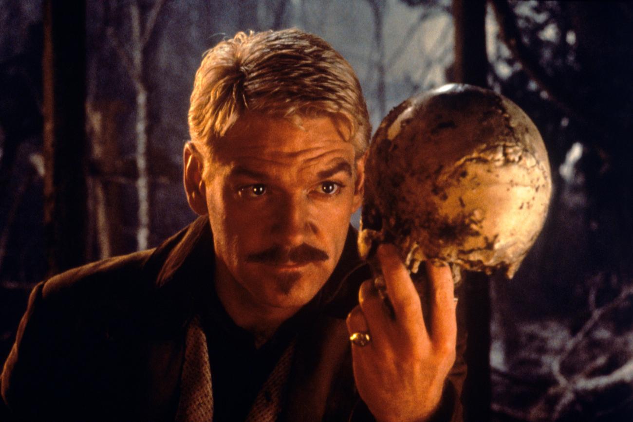The story title comes from Shakespeare: " The heart-ache and the thousand natural shocks / That flesh is heir to"—photo is of British actor Kenneth Branaugh holding a skull in the film Hamlet (1996). The photo shows the actor bathed in orange light and dressed in period garb holding a skull in a contemplative pose. GETTY IMAGES/Mondadori 