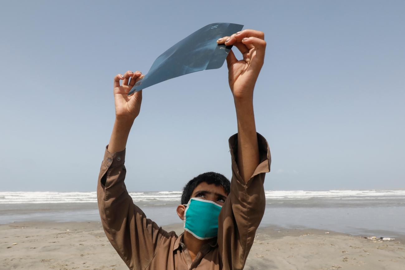 A boy holds an x-ray sheet as he observes the partial solar eclipse along Clifton beach, as the spread of the coronavirus disease (COVID-19) continues, in Karachi, Pakistan June 21, 2020.