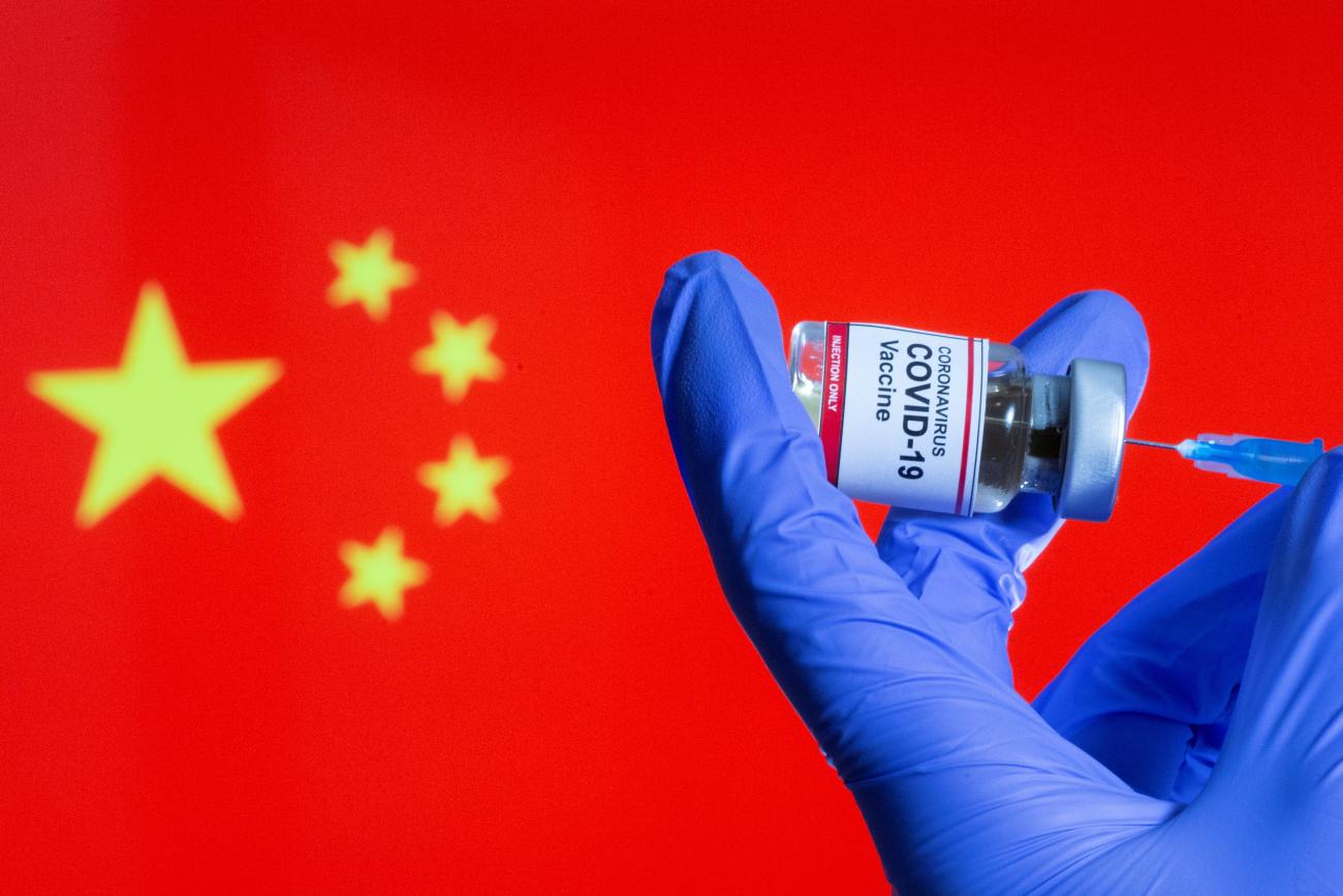 A woman holds a small bottle labeled with a "Coronavirus COVID-19 Vaccine" sticker and a medical syringe in front of displayed China flag in this illustration taken, October 30, 2020.