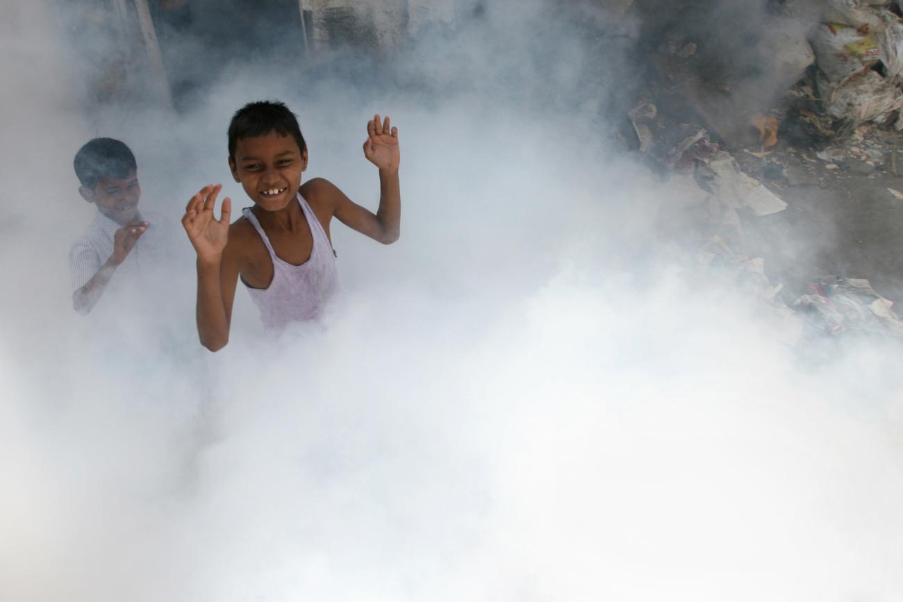 Children play as a health worker fumigates a residential area, where cases of malaria were reported, in Mumbai March 20, 2009. 
