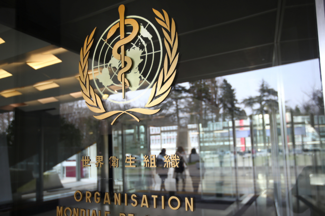 A gold World Health Organization logo in several languages on the glass door of a WHO building in Geneva in February 2021.