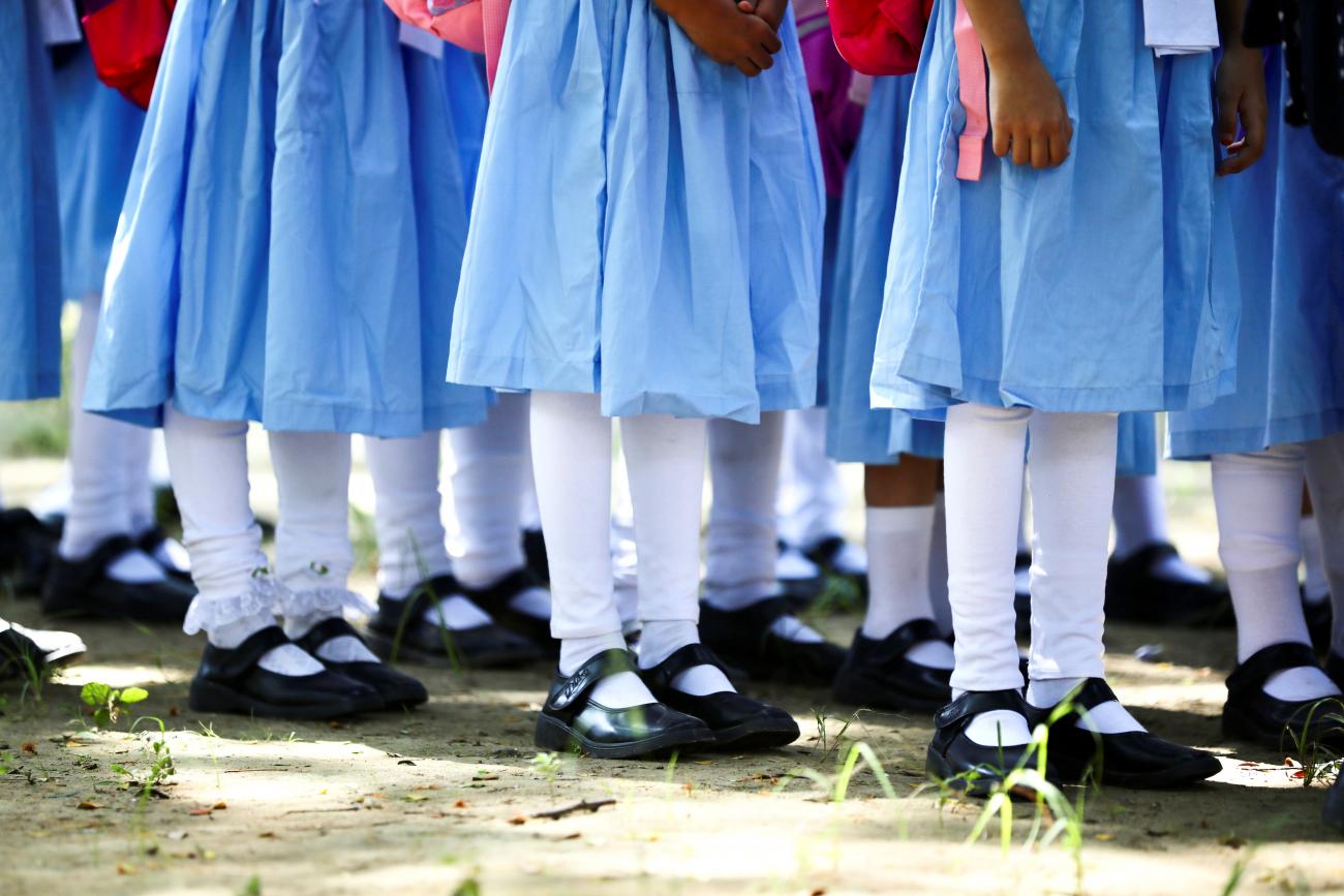 The legs and feet of students wearing blue dresses, white stockings, and black shoes can be seen standing in queues at the Viqarunnisa Noon School & College, in Dhaka, Bangladesh, September 12, 2021. 