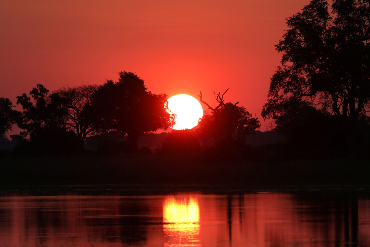 A brilliant orange-red sunset shimmers over the water and trees of tthe Okavango Delta, Botswana, on April 25, 2018. 