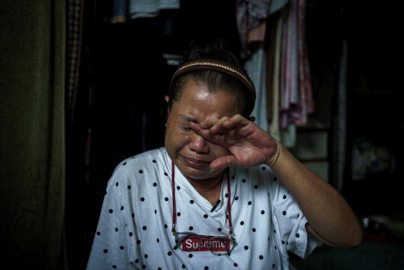 a woman wearing a white patterned t shirt wipes tears off her face