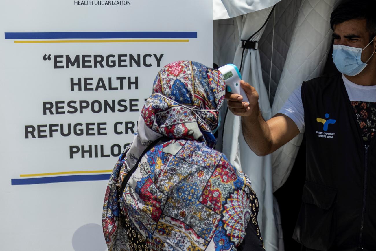 A health ministry official gets the temperature of a migrant before receiving the Johnson & Johnson vaccine against the coronavirus disease (COVID-19) in the Mavrovouni camp on the island of Lesbos, Greece, June 3, 2021.