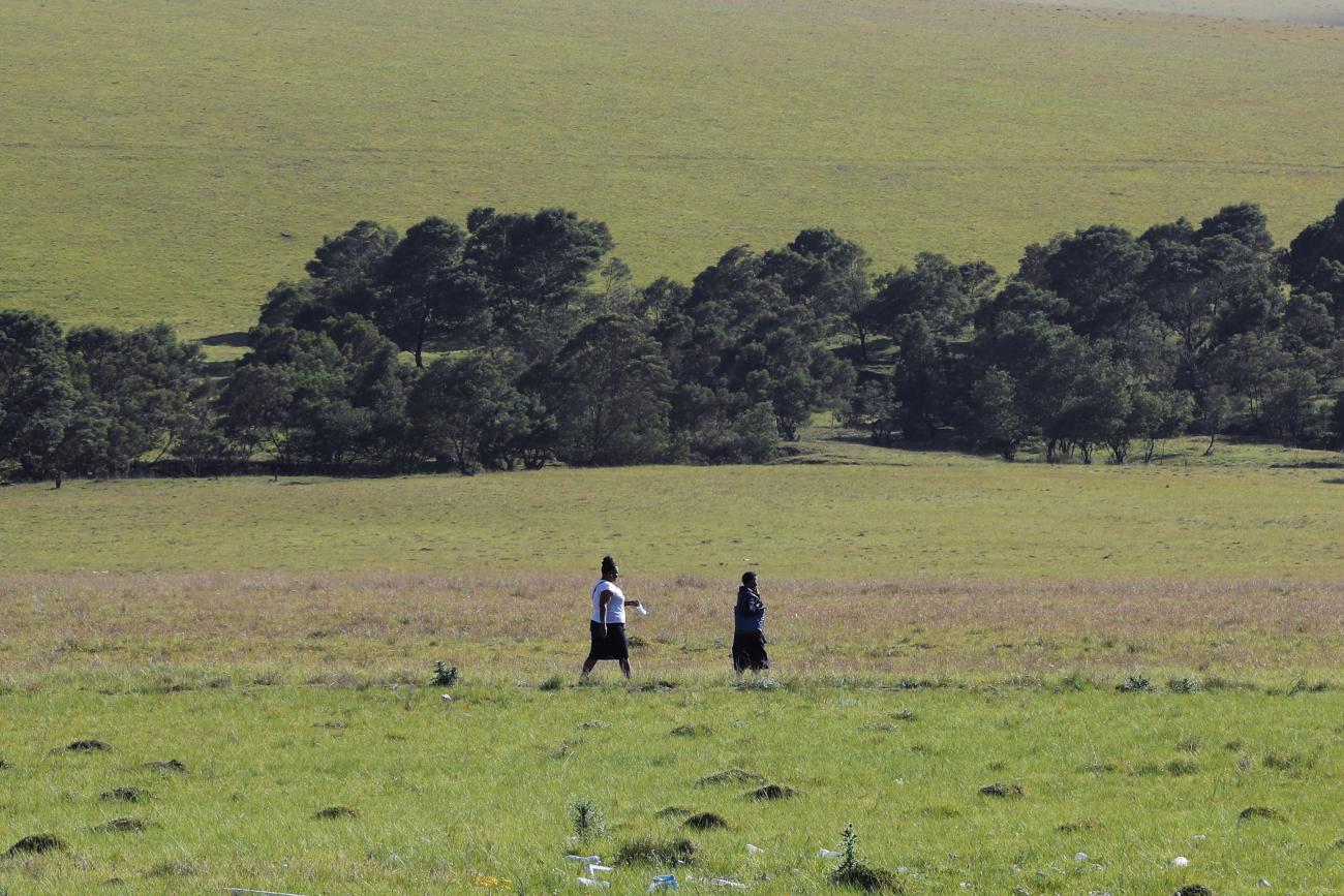 A green field and trees are the backdrop as two women walk, holding a face mask, in Dutywa, in the Eastern Cape province, South Africa, on November 29, 2021. News of the new COVID Omicron variant, now spreading in South Africa, was announced this week.