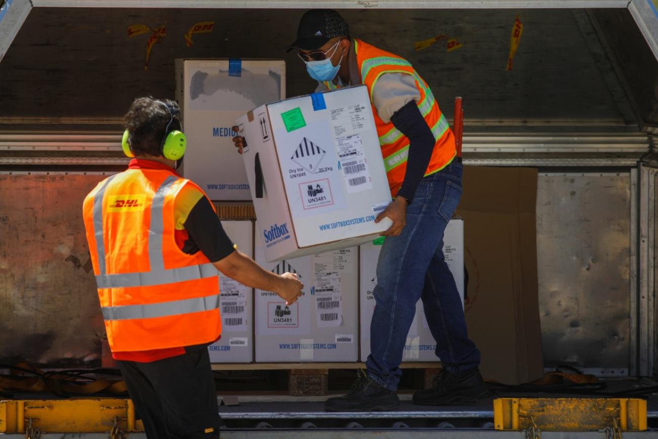 An air carrier worker in an orange vest transfers a box of Pfizer-BioNTech vaccine against the COVID-19 under the COVAX scheme at an airport in San Luis Talpa, El Salvador