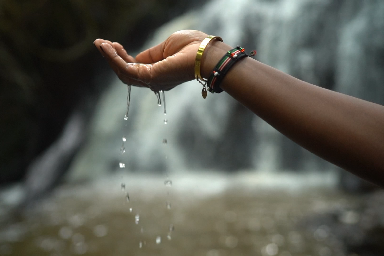 Dr. Liz Wangia lets water from a waterfall trickle from her hand in Nairobi National Park, Kenya