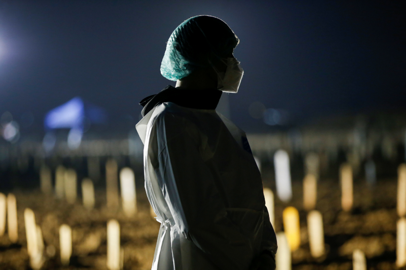 It is dark out as Toni Tanama awaits the funeral of his 51-year-old mother at a Muslim burial area provided by the government for COVID victims, in Jakarta, Indonesia, on July 7, 2021. In the background of his silhouette are rows of new gravestones reflecting the lights of the evening.