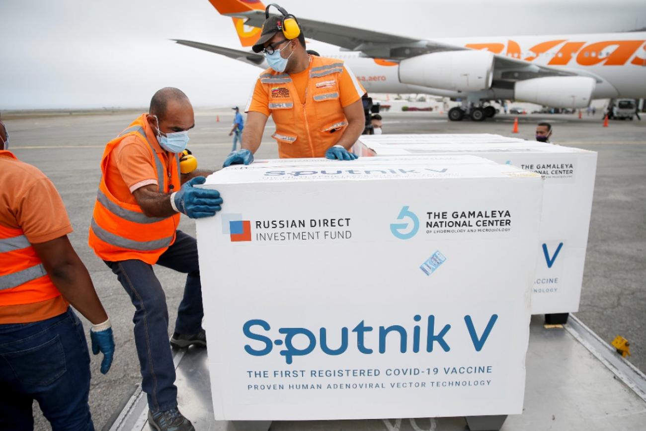 Workers in orange vests unload crates of Sputnik V at an airport in Caracas, Venezuela