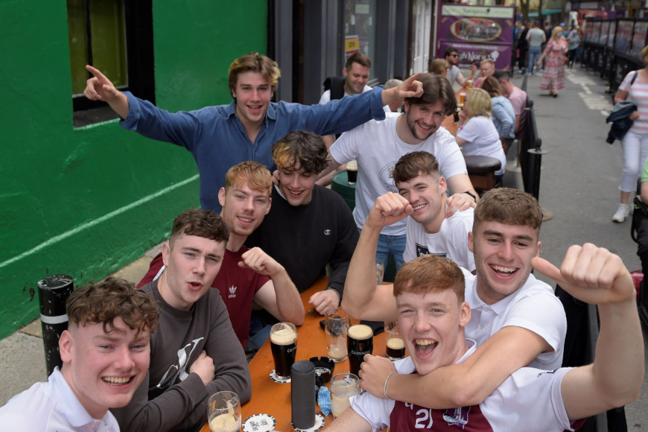 A group of young men cluster around a large outdoor table cheering, smiling, and drinking large glasses of beer as COVID-19 restrictions ease in Galway, Ireland, on June 7, 2021.