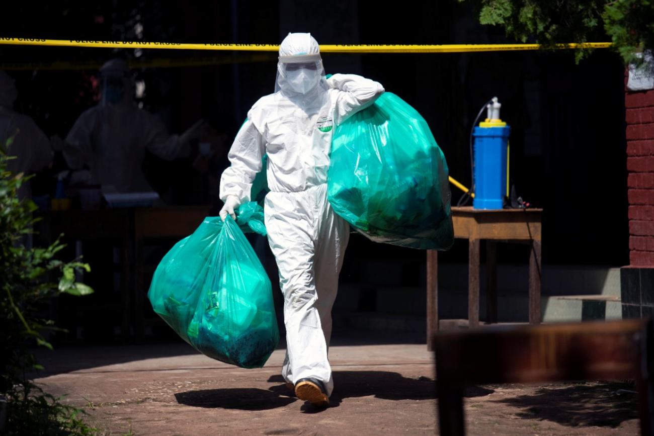 A medical worker carries green plastic bags of medical waste from a quarantine center in Myanmar during the COVIF-19 pandemic
