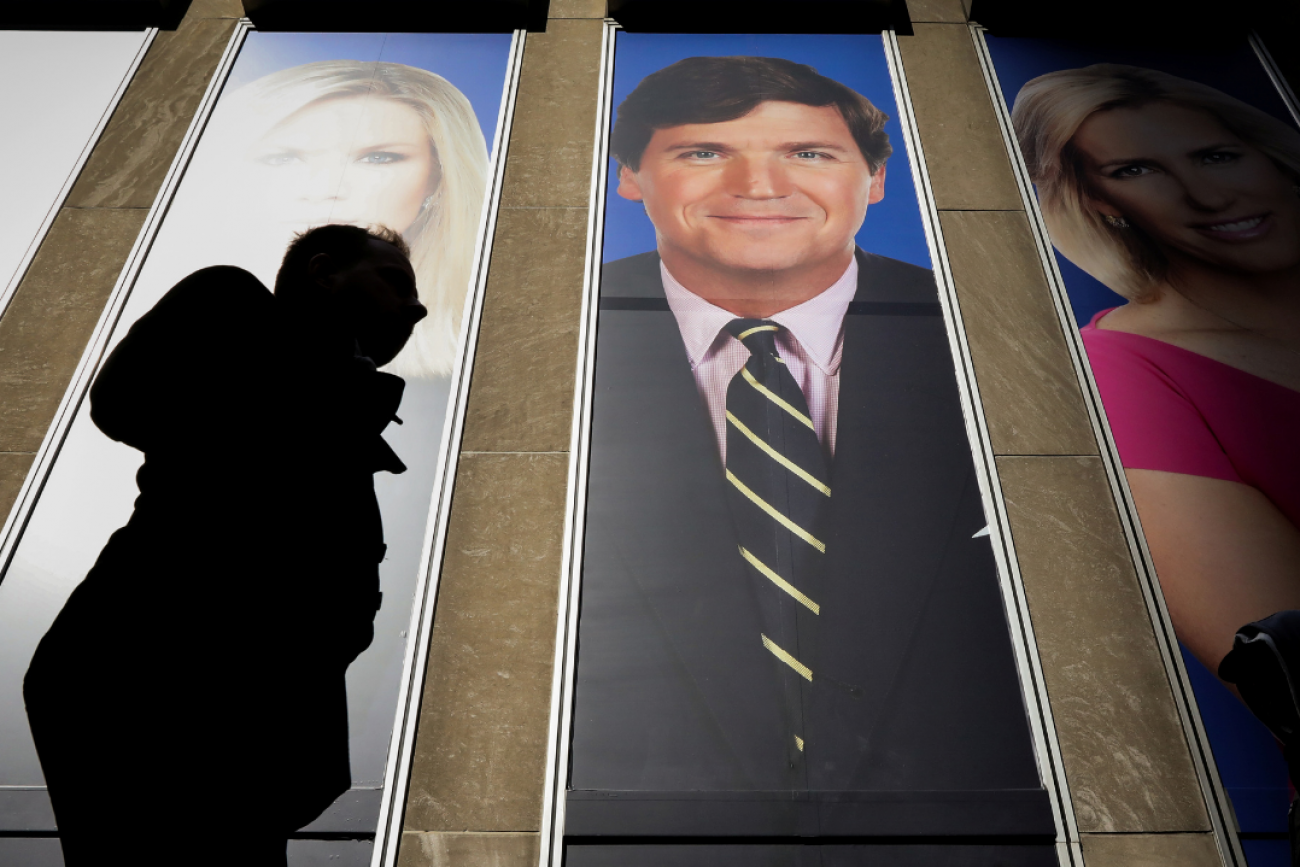 People pass by a promotional image of Fox News' Tucker Carlson on a building in New York, on March 13, 2019.