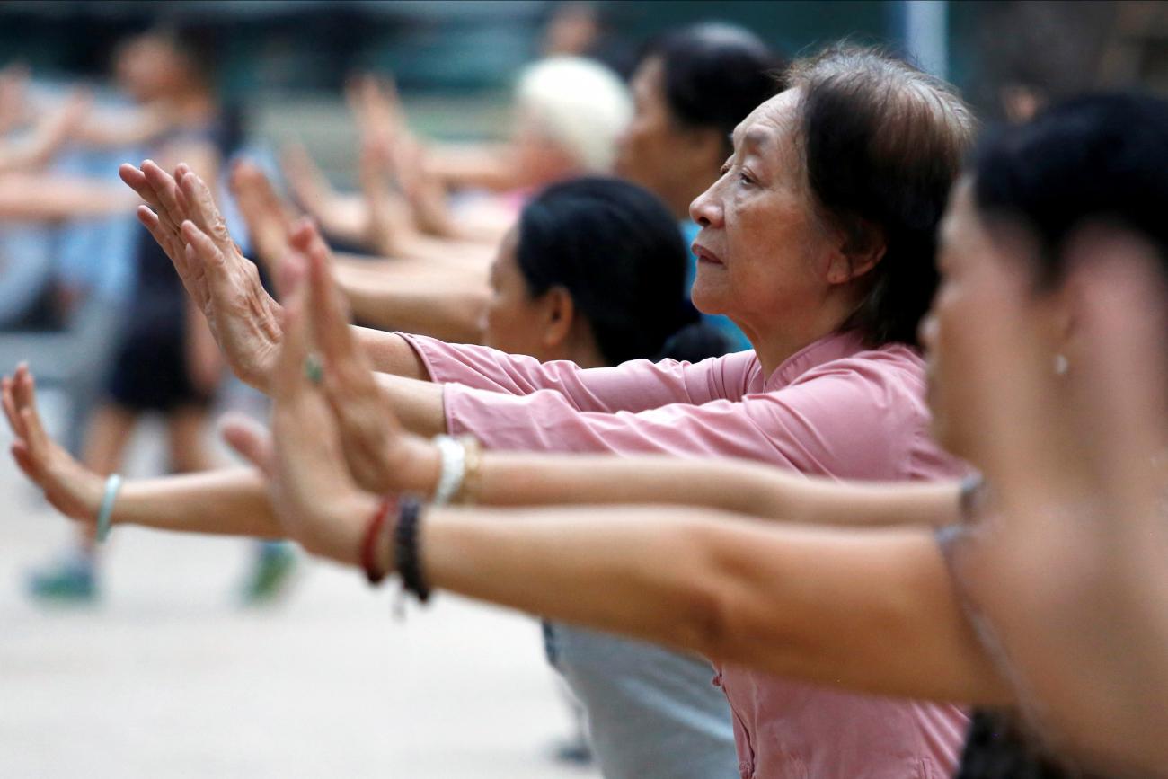 Elderly people stand in a row and stretch out their arms as they exercise at a public park in Hanoi, Vietnam on October 9, 2018.