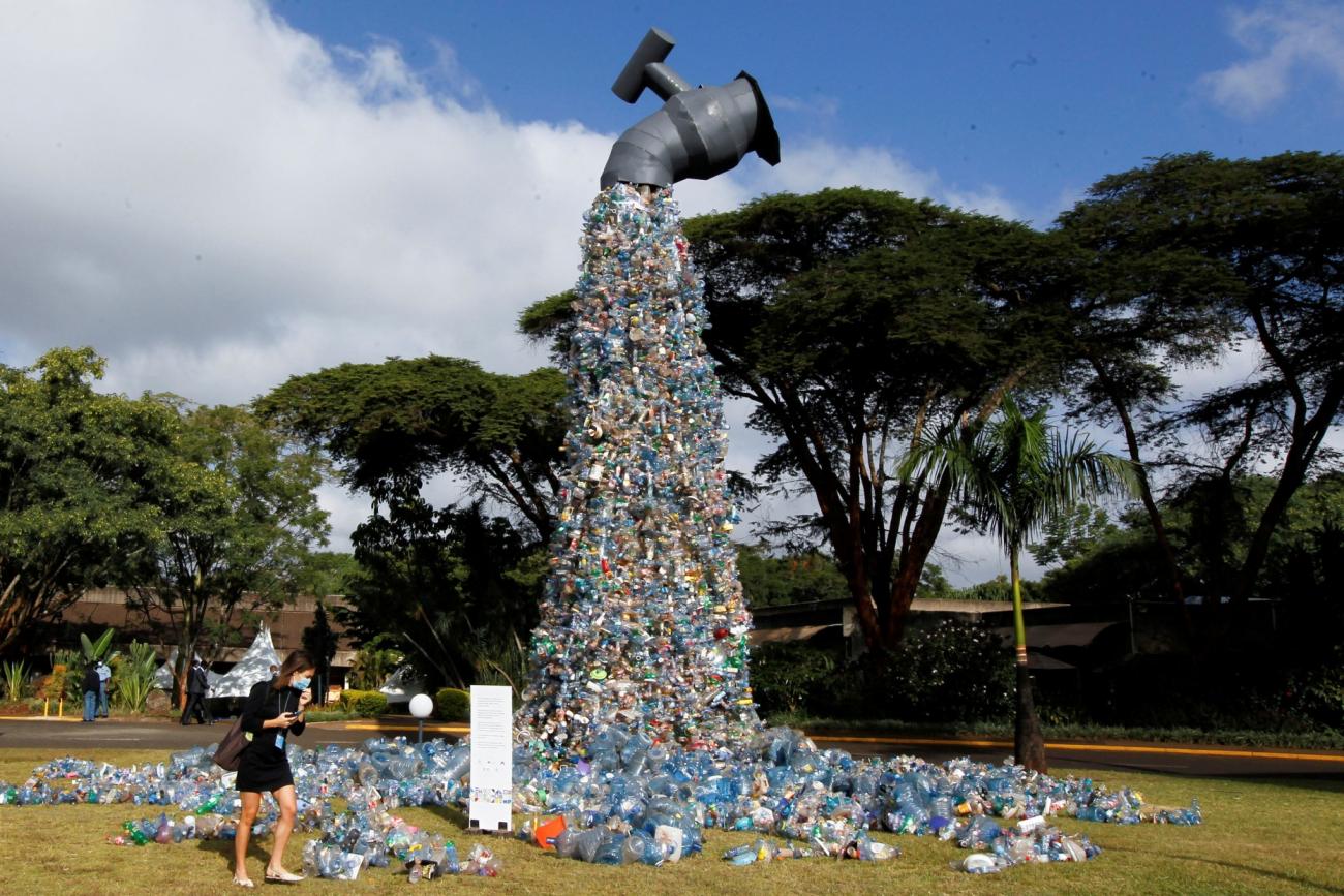 A female delegate wearing a long sleeved black dress a blue surgical mask looks at a 30-foot sculpture made out of plastic bottles resembling a faucet, outside the UN Environment Programme Headquarters, in Nairobi, Kenya 
