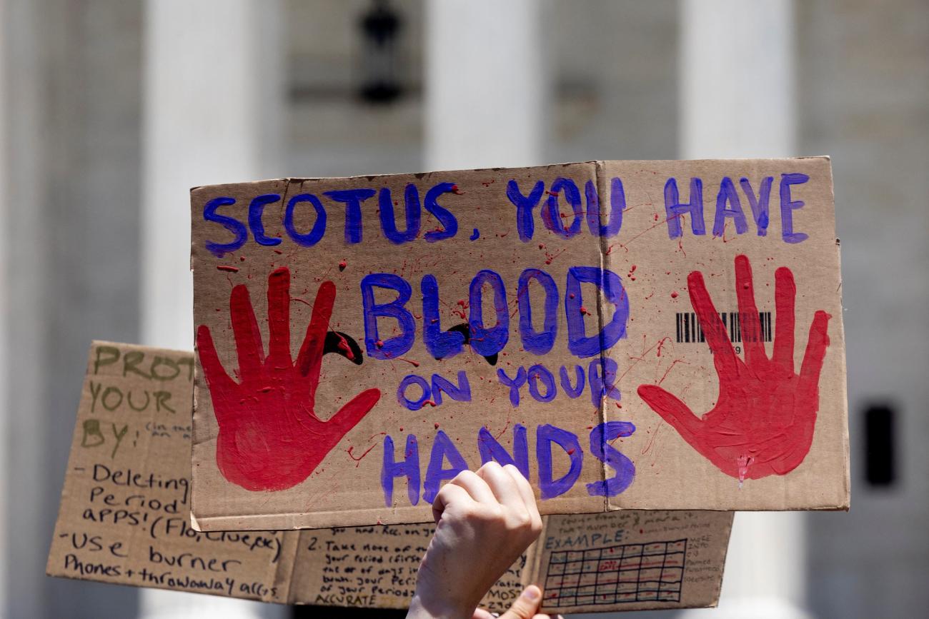 a cardboard signs reads "SCOTUS you have blood on your hands"