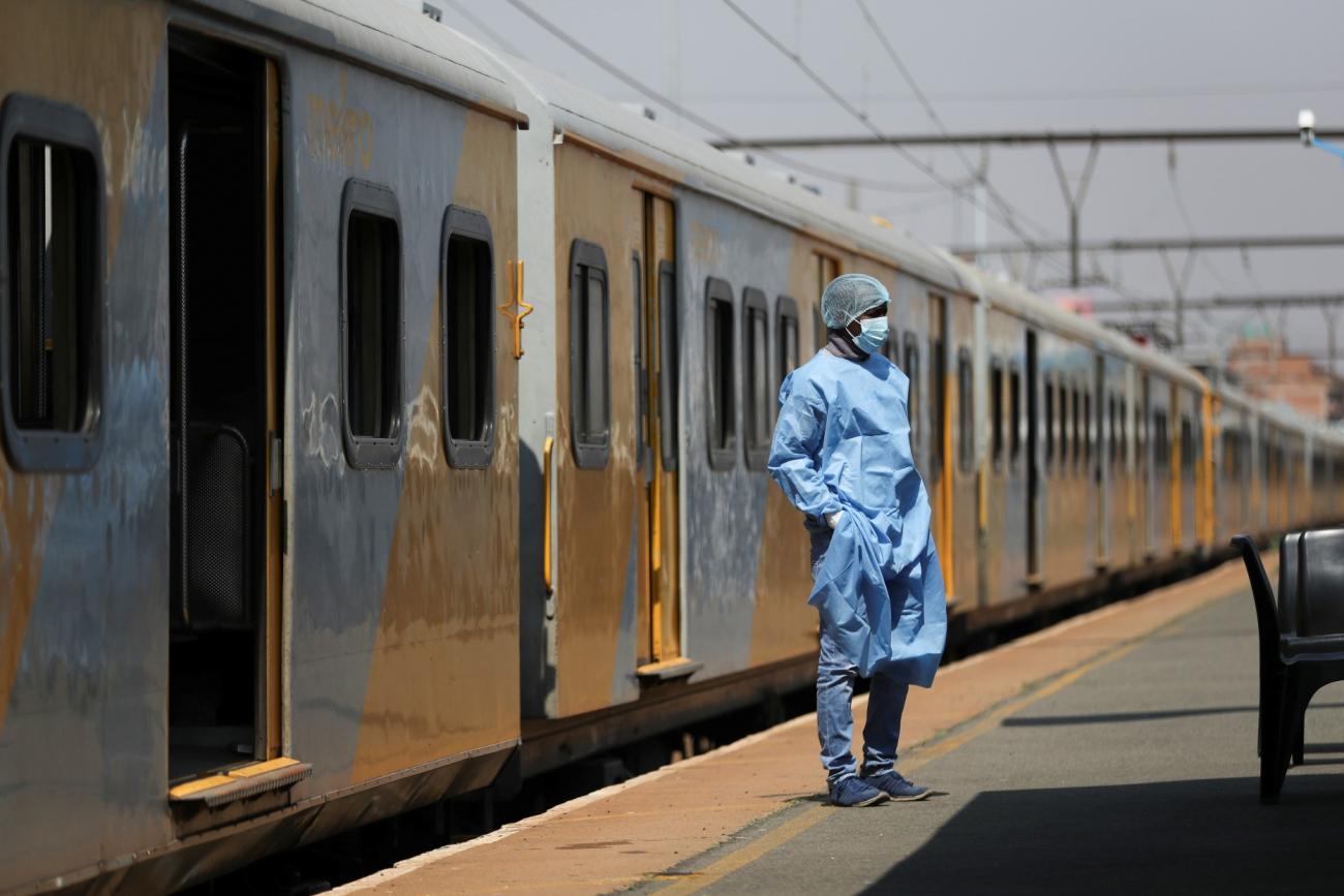 a health-care worker in blue scrubs and PPE stands in front of a train car